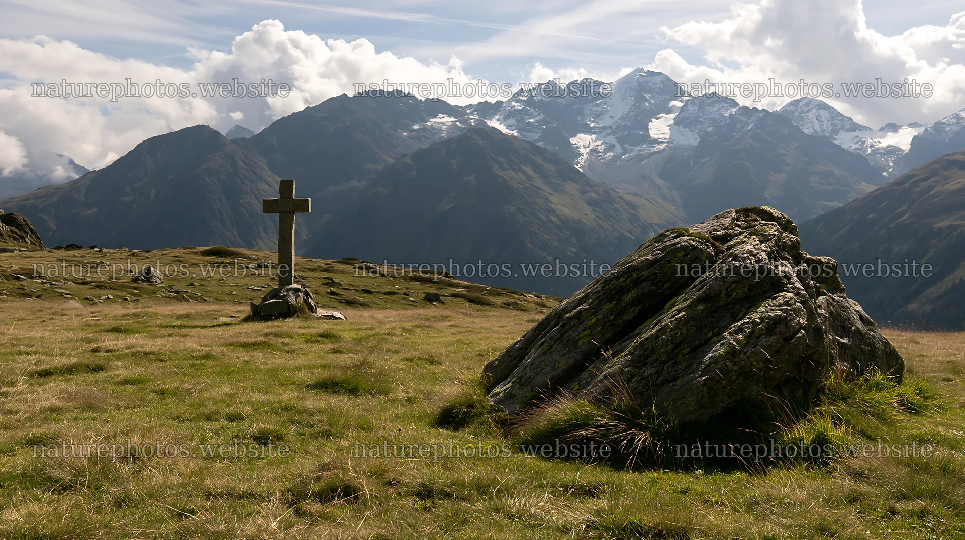 Stone Christian cross in alpine valley meadow – nature photos 10608x5938
